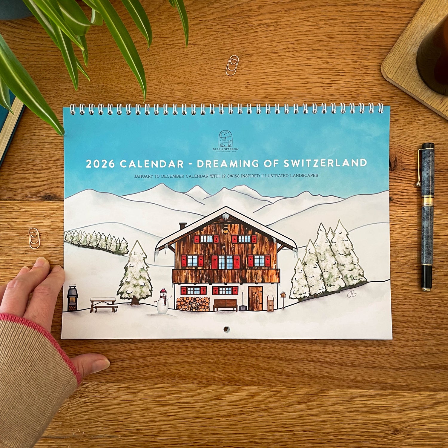 2026 Calendar titled 'Dreaming of Switzerland' on a wooden surface with a hand holding it.